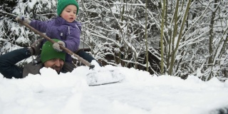 一场大雪过后，可爱的小男孩坐在爸爸的肩膀上，用刷子从积雪覆盖的车顶上铲雪。
