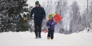 父亲和儿子在暴风雪中拿着雪铲对着摄像机在乡村公路上奔跑。