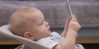 可爱的白人小孩坐在摇椅上看动画片，9个月大的婴儿抱着平板电脑在家。儿童和移动技术。