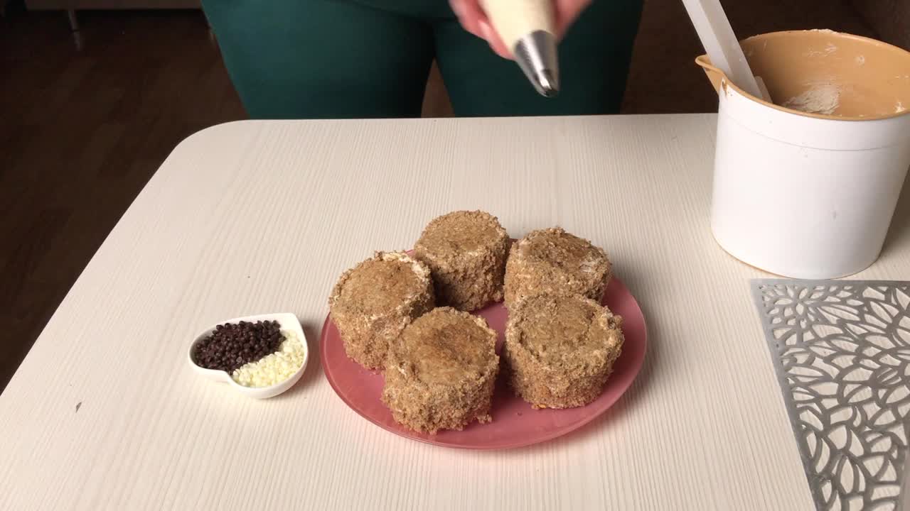 一位女士用奶油和饼干屑做海绵蛋糕。用糕点袋装饰奶油。总体规划。