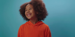 微笑的非裔美国女孩的肖像在橙色的衣服看着镜头在蓝色的背景。7岁快乐小孩的特写。