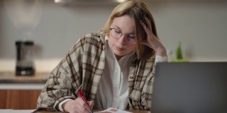 这位女士在家远程工作，坐在桌子旁，用笔记本电脑和毡尖笔在图表上标记数据。紧张地在视频上说话
