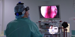 医生背对着镜头，看着屏幕。进行手术的外科医生看着屏幕上显示的内部器官。关闭了。