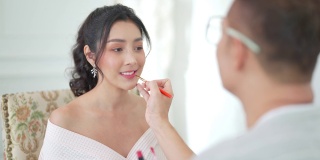 4K亚洲男化妆师为身着白色婚纱的新娘化妆。