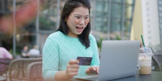 微笑的亚洲妇女使用智能手机和信用卡管理网上银行，坐在阳台花园的夜光。网上购物让生活更容易，生活方式和技术