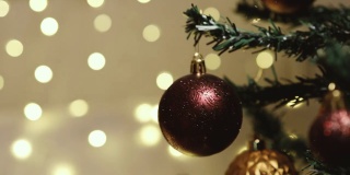 圣诞快乐，恭贺新禧。女性的手用酒红色的球和玩具装饰圣诞树，在装饰好的房子里准备新年假期。