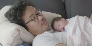 4k幸福疲惫的亚洲父亲和儿子睡在沙发上早上。