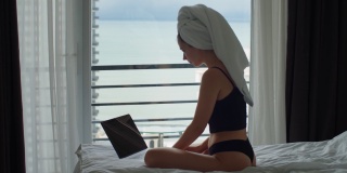 有魅力的女人在网络上工作，早上看着窗外。美丽的女孩自由职业者在床上打字笔记本电脑检查电子邮件或新闻。隔离期间的晨间常规