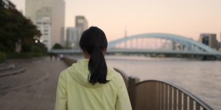 落日时分，东京，一名女子在河边奔跑的背影