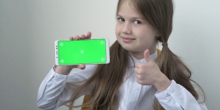 一名穿着白色上衣的女学生用绿色屏幕模拟手机、手机、电话。绿屏智能手机的色度键设置为广告。教育、科技、小玩意和孩子