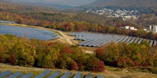 宾夕法尼亚州阿巴拉契亚山脉的大型太阳能农场，在一个多彩的秋天。空中视频与前向摄像机运动。