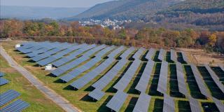 宾夕法尼亚州阿巴拉契亚山脉的大型太阳能农场，在一个多彩的秋天。空中视频与前进和上升的摄像机运动。