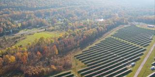 宾夕法尼亚州阿巴拉契亚山脉的大型太阳能农场，在一个多彩的秋天。航拍视频与宽平移轨道摄像机运动。