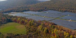 宾夕法尼亚州阿巴拉契亚山脉的大型太阳能农场，在一个多彩的秋天。空中加速视频与广泛的全轨道，前摇复杂的电影摄像机运动。