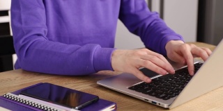 年轻的成年女性穿着紫色连帽衫在笔记本电脑上。在家工作的概念