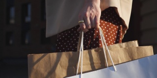 年轻的女顾客拿着购物袋走在人行道上。时尚的女人拿着纸包走在城市的街道上。休闲和自由时间的概念。起重机镜头