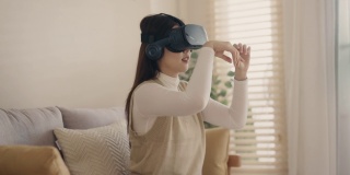 年轻貌美的亚洲女子戴着VR眼镜坐在家里的沙发上。