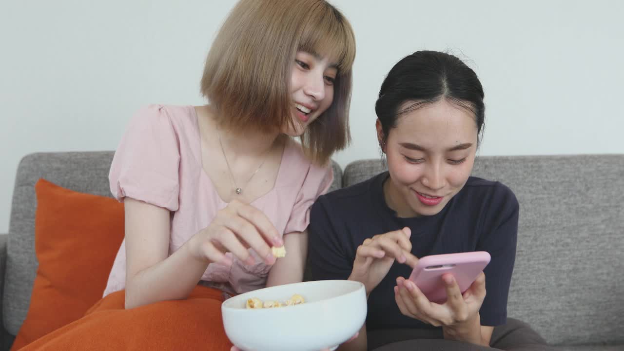 两个女人坐在家里的沙发上吃着零食聊天，享受着假期的欢笑。