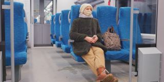 成熟的女人戴着口罩，坐着客运列车。她会拿着智能手机，在通勤途中查看社交媒体，阅读在线新闻。