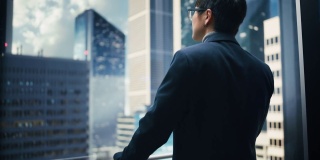 时尚的日本商人乘坐玻璃电梯到现代商务中心的办公室。从电梯的全景窗口看现代市中心的摩天大楼。转身对着镜头。
