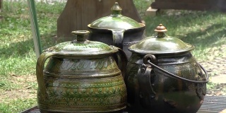 三个上釉的绿色陶瓷锅在一个很受欢迎的集市上的金属烤架上煮食物，人们在那里步行参观展品
