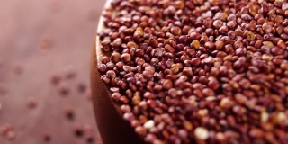 红色藜麦在乡村碗木制厨房板。以慢动作落下原粮。宏