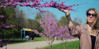 春天，美丽的女人在公园里散步，欣赏粉红色的樱花
