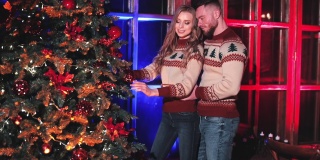 圣诞树旁穿着冬衣的幸福夫妇。恋爱中的年轻人站在新年树旁。晚上在家的浪漫气氛。
