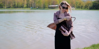 一个美丽的年轻女子在湖边的公园里，为了让自己更漂亮，她正在手提包里找一面镜子