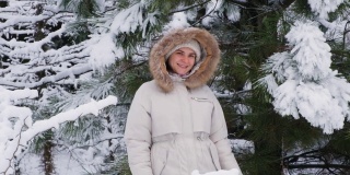 女视频人像慢镜头拍摄，一名女子在冬天的雪原林里微笑着看着镜头，雪花飞舞而过。