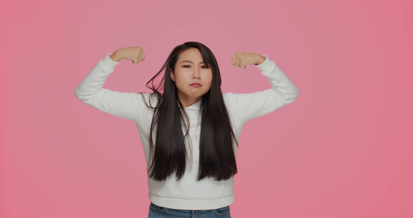 自信的亚洲女孩展示力量和力量，举起手臂展示二头肌，亲吻肌肉自豪的成就