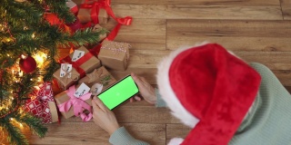 女性红色圣诞帽智能手机手绿屏下冷杉树礼盒