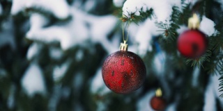 红色球玩具装饰在圣诞树上的特写与模糊的雪背景。圣诞快乐，节日快乐