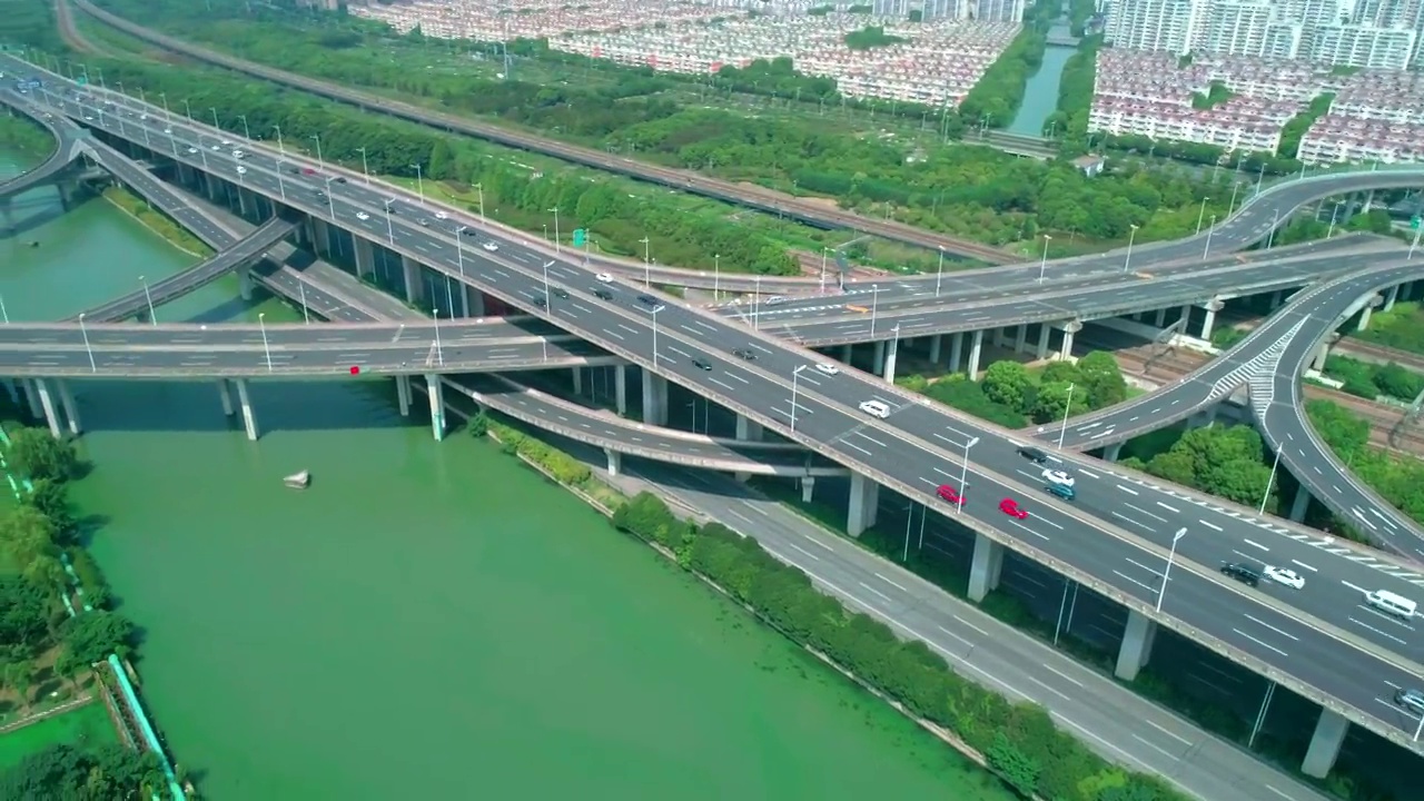 空中轨道视图的高速公路立交桥多层路口，快速移动的汽车被绿树包围，在一个阳光明媚的日子里，有一条河在一边