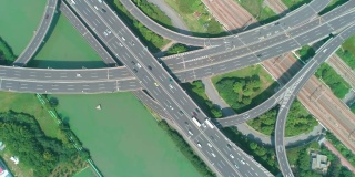 从空中俯瞰高速公路立交桥多层路口，快速移动的汽车被绿树环绕，在阳光明媚的一天，有一条河在一边。