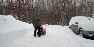 在一场冬季暴风雪后，一名男子正在清理他的汽车周围被雪覆盖的车道。启动snow-thrower。