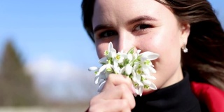 美丽微笑的黑发女孩捧着雪花花束第一春的花。