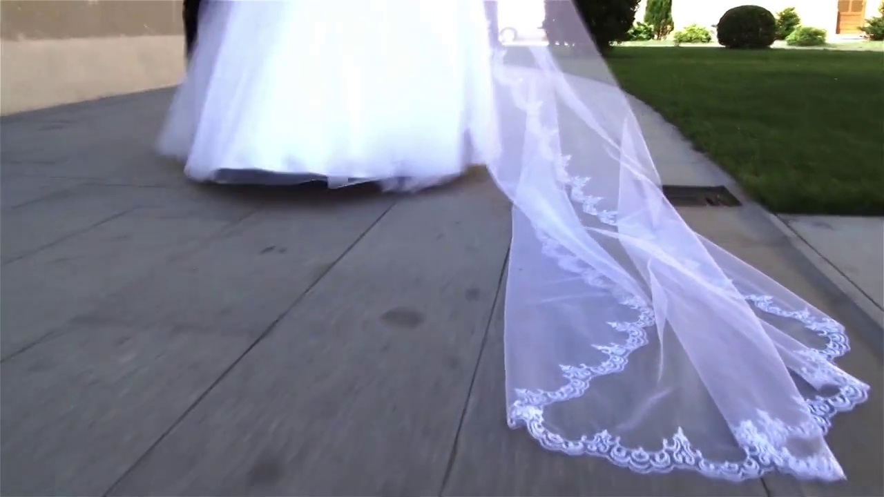 新娘的面纱拖在水泥车道上，后面是一个身穿白色礼服的女人
