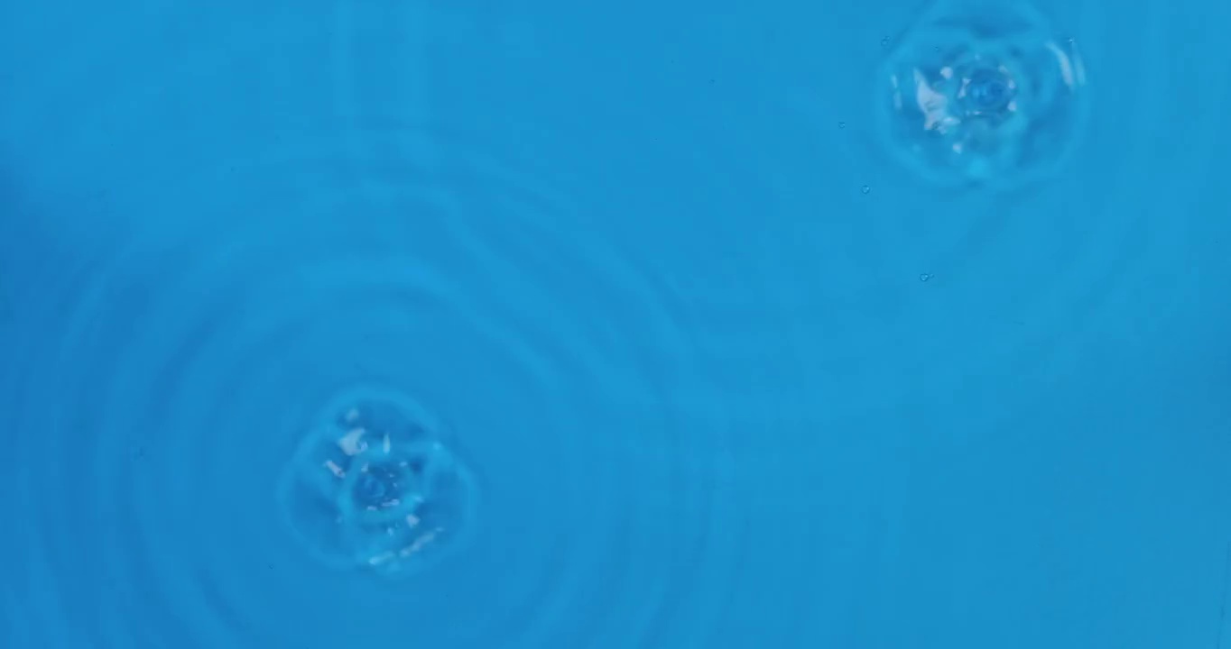 两滴雨落在蓝色的水中。前视图。水滴落入水中，形成水圈