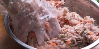 妇女双手戴着一次性塑料手套，将生腌猪排、胡萝卜丁、大葱和小香菇片与调料混合在碗里，准备烹饪。