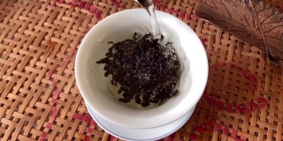 如何泡中国乌龙茶。热水从高处冲下，铁观音茶叶的颗粒在水中旋转，形成一个漩涡。茶碗里的白茶。缓慢的运动。