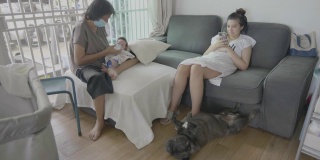 奶奶和女儿在客厅的沙发上给喝牛奶的孙子喂奶，旁边还有一只法国黑斗牛犬。