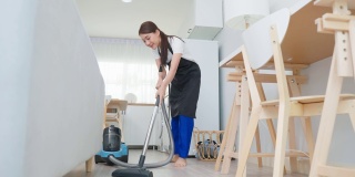 亚洲清洁服务女工清洁客厅在家里。美丽的年轻女孩管家清洁工穿围裙和吸尘肮脏的地板，家务和家务在房子。
