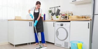 亚洲主动清洁服务女工清洁厨房和家庭。美丽的年轻女孩管家清洁工感到高兴，在地板上拖地工作，家务或家务在家里。