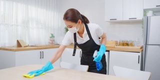 亚洲主动清洁服务女工清洁厨房和家庭。年轻漂亮的女管家清洁工戴上口罩，心情愉快地擦拭着脏乱的桌子，为家政做家务或杂务