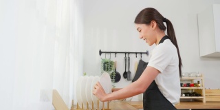 亚洲主动清洁服务女工清洁厨房和家庭。美丽的年轻女孩管家清洁工感到高兴，并擦拭盘子洗后的家务或家务。