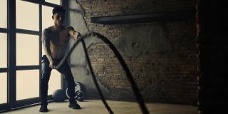 健身男用废弃仓库的战绳锻炼身体。硬汉在旧工厂内的交叉训练馆锻炼。健身房，健身，健身，训练，锻炼，健身，运动，生活方式，健康俱乐部，