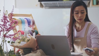 亚裔女性花商，小型商业花店老板，在笔记本电脑上工作对花卉和植物。查看库存，接受客户订单，在线销售产品。用科技经营小生意的日常工作视频素材模板下载