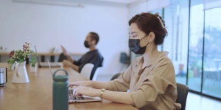亚洲女商人戴着口罩在笔记本电脑上工作