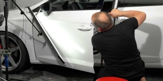 汽车修理厂左车门表面凹痕的修补工艺。技术员正在使用工具进行无漆凹痕修复。